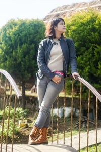 Young woman looking away while leaning on railing against trees