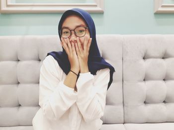 Portrait of young woman wearing hijab sitting on sofa at home