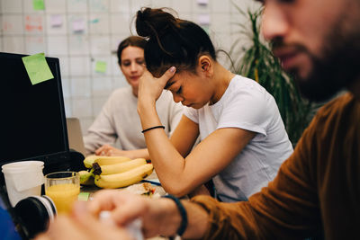 Worried businesswoman sitting amidst colleagues at desk in creative office