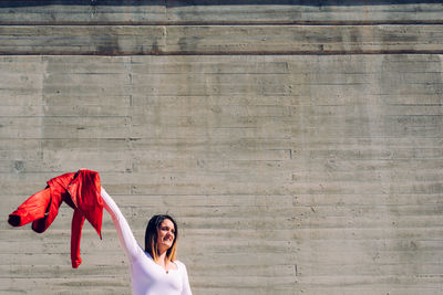 Beautiful woman holding jacket while standing against wall