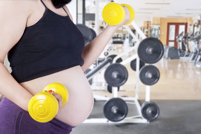 Midsection of pregnant woman lifting dumbbells at gym