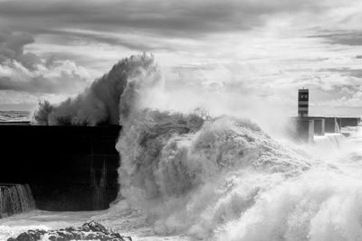 Sea waves splashing on groyne against sky