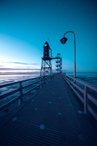 Street lights on pier by sea against blue sky