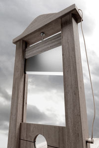 Low angle view of guillotine against cloudy sky