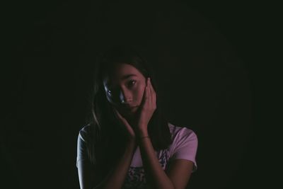 Portrait of young woman against black background