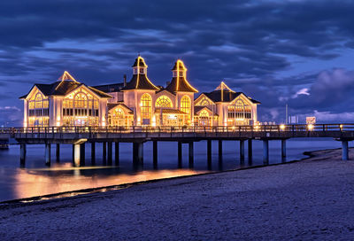 Illuminated building by sea against sky at night
