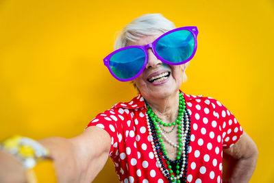 Portrait of cheerful young woman wearing sunglasses against yellow background