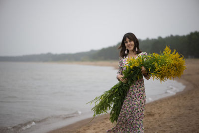 Young beautiful woman with a large bouquet of wild flowers posing on the beach