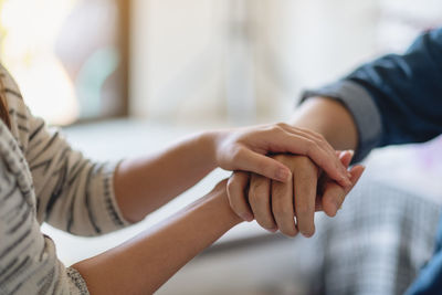 Midsection of couple holding hands at home