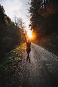 Rear view of woman with arms raised standing on road in forest