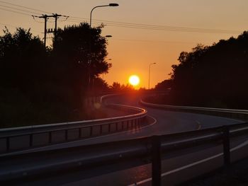 Road by silhouette trees against sky during sunset