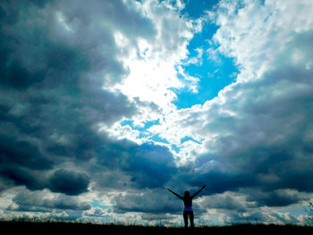 Silhouette of person with arms raised against cloudy sky
