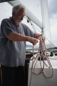 Senior man working on sailboat against sky