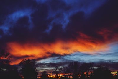 Low angle view of silhouette trees against dramatic sky