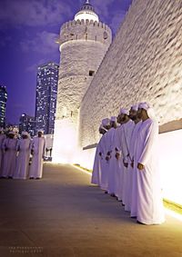 Rear view of people walking by building against sky