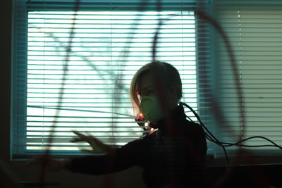 Woman wearing mask while standing by window