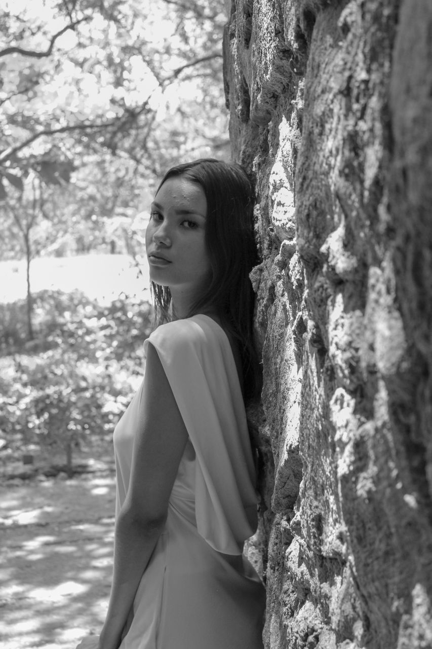 SIDE VIEW OF YOUNG WOMAN STANDING AGAINST TREES