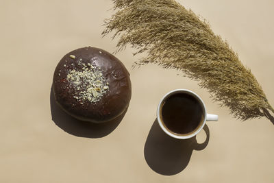 Cup of black coffee with chocolate loaf on a beige background with hard shadows 