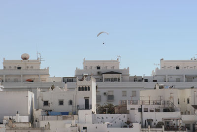 Paraglider above building in city against clear sky