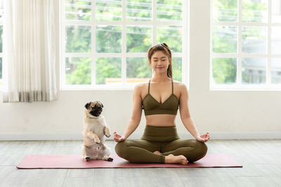 Full length of woman meditating with dog at home