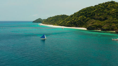 Sailing yacht in crystal clear turquoise water right next to the white sand beach of tropical island