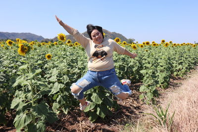 Portrait of smiling woman jumping by sunflower field against clear sky