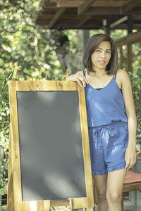 Portrait of young woman standing by blackboard