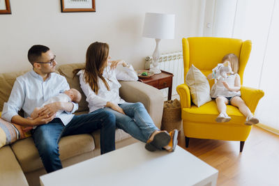 Father with newborn son in yellow armchair. family of four. dad son mom and daughter