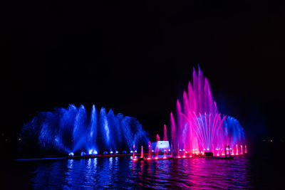 Illuminated firework display over river against sky at night