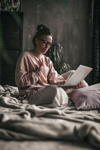 Midsection of woman using mobile phone while sitting on bed