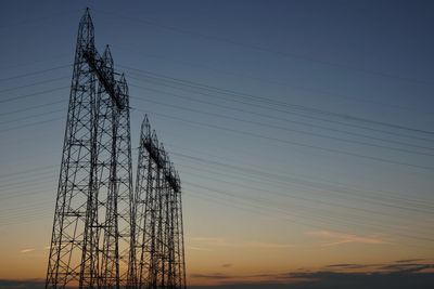 Low angle view of silhouette electricity pylon against sky during sunset