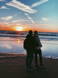 Couple standing on beach against sky during sunset