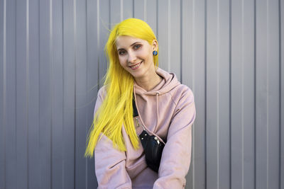 Portrait of a smiling young woman standing against wall