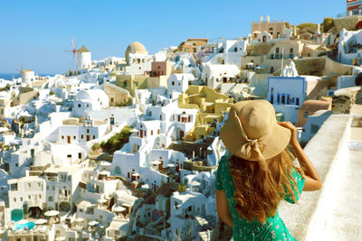 Rear view of young woman looking at cityscape against clear blue sky during sunny day