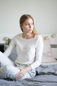 Portrait of young woman sitting on bed at home