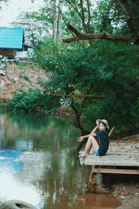 Boy sitting by lake against trees
