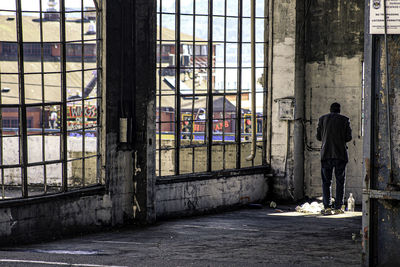 Rear view of man standing by window in abandoned building / homelessness from the outside looking in 