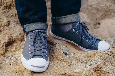 Low section of man wearing shoes standing on sand at beach