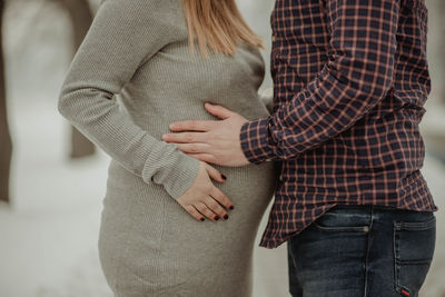 Midsection of man touching pregnant woman stomach while standing outdoors