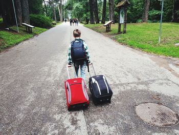 Rear view of boy pulling luggage on road