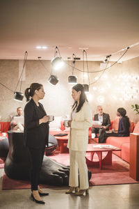 Full length of businesswomen talking during coffee break while coworkers sitting in background