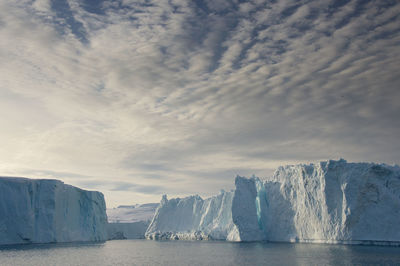 Ice formations in sea against cloudy sky