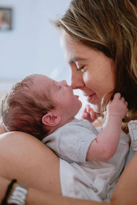 Closeup of loving mother holding adorable newborn baby while sitting on bed at home