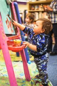 Side view full length of baby boy painting at library