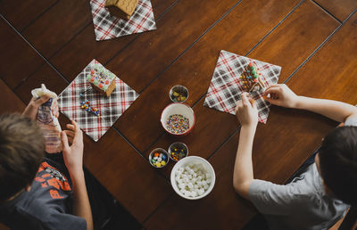 Overhead shot of two boys decorating gingerbread houses on a table.