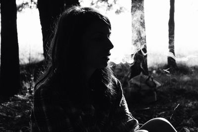 Woman smoking cigarette while sitting against trees