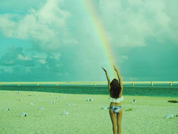 Rear view of woman standing against rainbow at beach