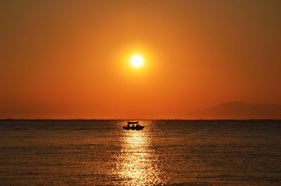 Red orange sun and a silhouette of a boat in the middle of the sea