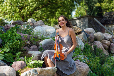 Beautiful brunette in a linen dress with a violin on a pile of boulders at an old country house