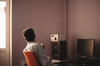 Man looking through window while sitting by desktop computer